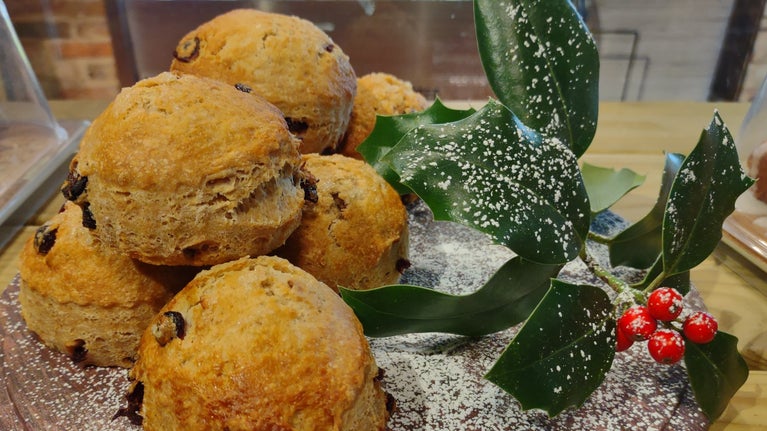 Christmas pudding scones at Treasurer's House, York, piled on a wooden board and dusted with icing sugar, with a sprig of holly alongside